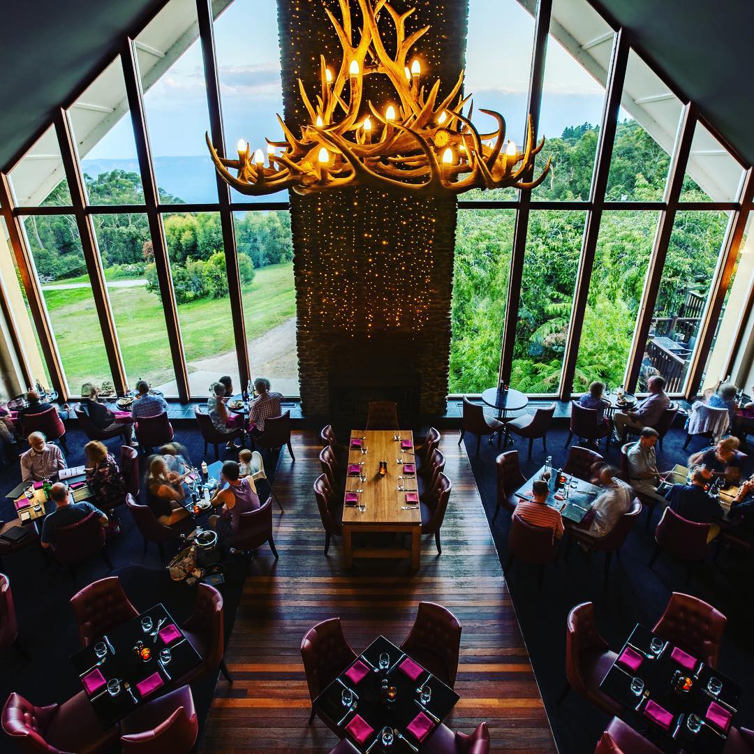 Photo of the dinning area in the main building of the Fairmont Resort. There is a large chandelier in the shape of antlers with a view of the garden and valley.
