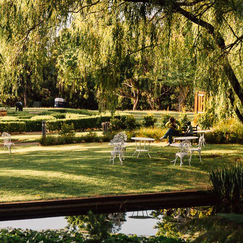 Photo of a garden area at the Fairmont Resort. There is an antique table and chairs under some trees.